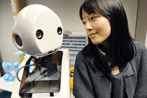 Professor Min Kyung Lee smiling at the face of white robot 