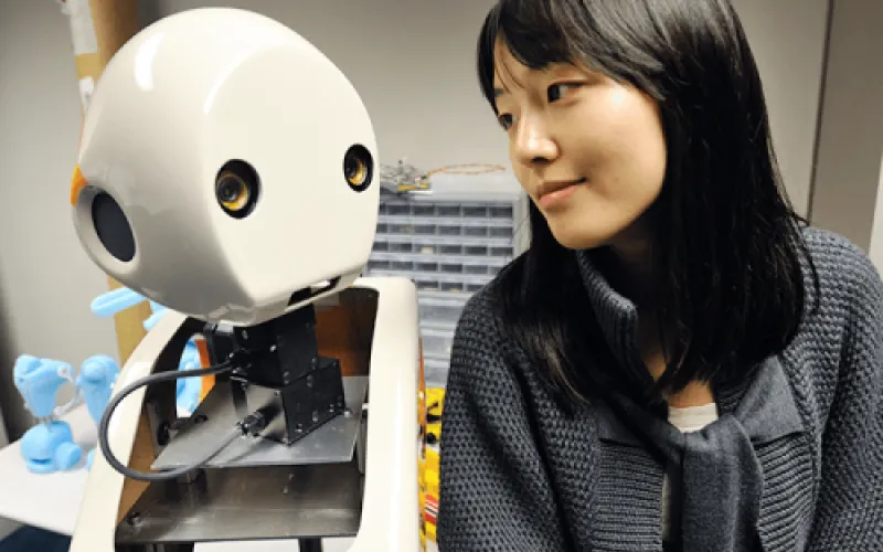 A picture of Dr.Min Kyung Lee sitting next to a robot