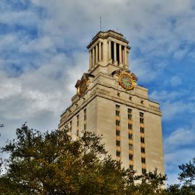 The UT University of Texas tower rising above trees against a blue sky with white clouds