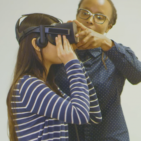 Professor Jakki Bailey assists a student wearing a VR headset in class